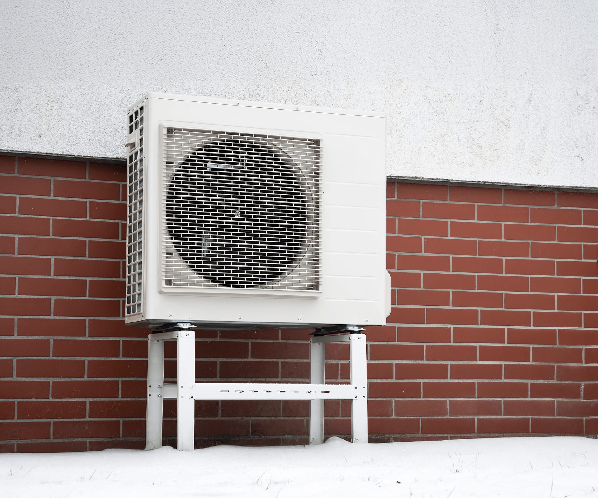 thermopompe extérieure en hiver dans la neige contre un mur de brique
